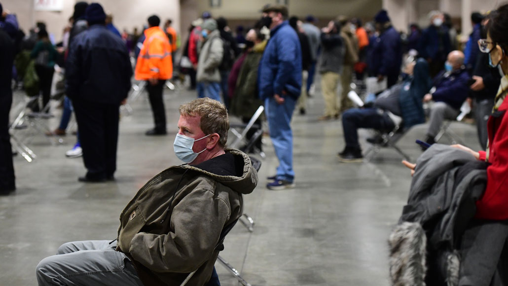 image of people siting and standing in line to get doses of the COVID-19 vaccine