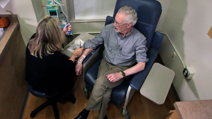 man sitting in a chair receives an infusion of aducanumab
