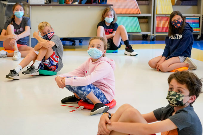 group of young children sitting on the floor, spread out and wearing masks