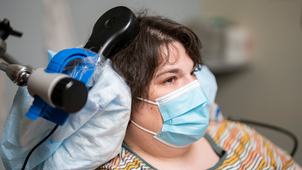 woman wearing face mask with medical device applied to her head; the device measures brain activity