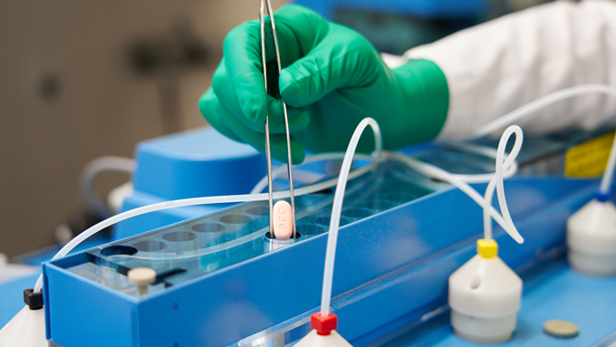 image of a hand holding a Paxlovid pill with tweezers
