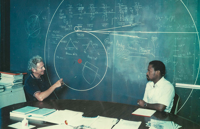 Leon Lederman talks to Sekazi Mtingwa in front of a chalkboard