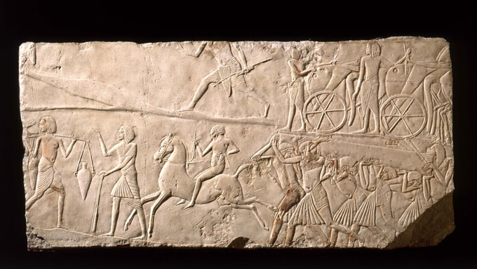 An ancient Egyptian limestone relief showing a person on horseback among workers doing various things.