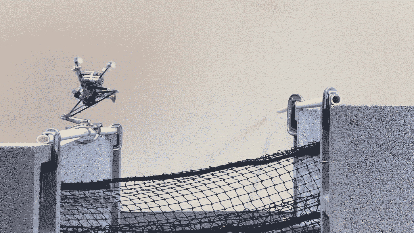 A jumping robot with one leg leaps from one PVC pipe to another. A black net is strung below it.