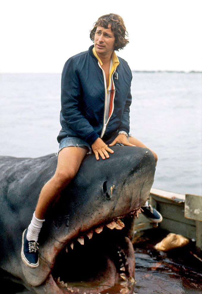 A 1970s photograph shows Jaws director Steven Spielberg sitting on top of a life-sized mechanical shark that's in water