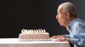 An elderly man in a blue collared shirt and bowtie leans over the edge of a table to blow out dozens of candles on a birthday cake. Elderly, healthy adults might benefit from brain mapping to detect early signs of depression and Alzheimer’s disease.