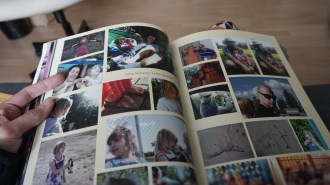 A person's hand holding an open photo album with its pages full of pictures, some labelled "Early summer in the backyard."