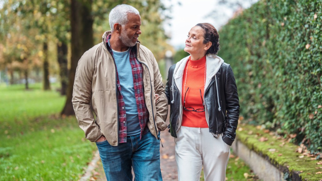 Two older people walk on a foliage-lined path.