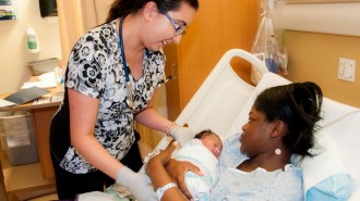A nurse helps a mother in a hospital bed hold her newborn baby.